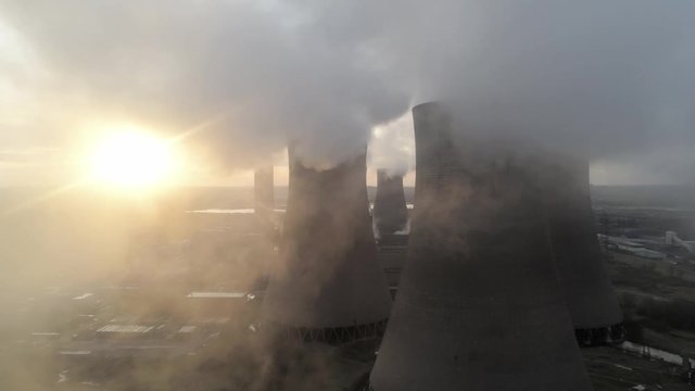 Aerial view of UK power station cooling towers glowing smoke fly through emissions at sunrise.