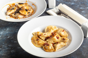 Dumplings and ravioli stuffed with meat. Sprinkle sliced smoked tomatoes. Served on a large white plate. Next to a bowl of sour cream. On a wooden background.