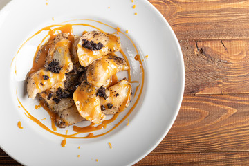 Ravioli stuffed with cottage cheese and poppy seeds. Served with poppy seeds and caramel sauce. On a large white plate. On a wooden background.