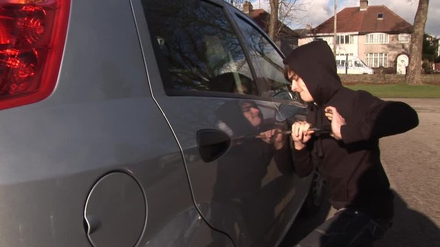 Criminal breaking into a Car. The Thief is using a crow bar to open the door. The burglar is a young male - Stock Video Clip Footage