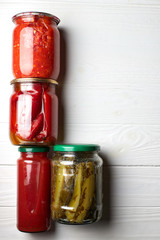 Preserved vegetables in jars, ont a white background. Cucumbers, bell pepper, adjika, tomato juice