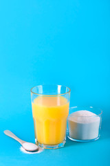 A glass juice and a spoon with collagen powder on blue background.