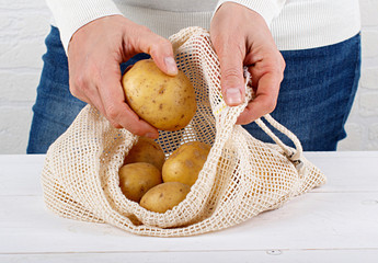 Woman put fresh potatoes in a textile bag