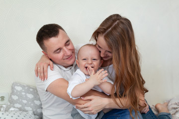 Portrait of a happy young family. Parents and baby hugging and playing on the sofa in the room