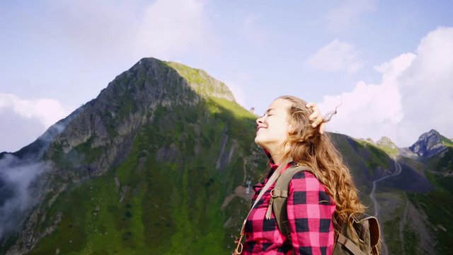 Young woman walking in mountain. Headshot girl rising arms up in winner gesture, celebrates the ascent while standing on top of peak and enjoying scenic nature landscape. Travel adventure concept