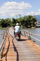 man rides a motorcycle on a wooden bridge over the river