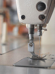 Needle presser foot with brown thread of white industrial sewing machine use sew cloth close-up.