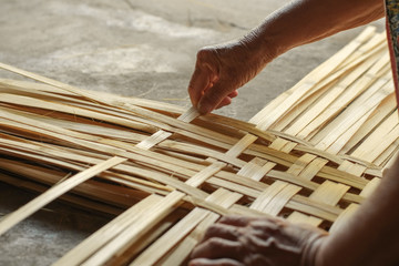 Hand elderly woman are weave bamboo strips of bottom of basket.