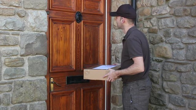 Courier / Delivery man delivering a parcel at house / home. A woman open the front door and takes delivery of the package. Tracking Shot. Stock Video Clip Footage