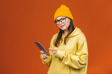 Smiling young woman using tablet computer isolated on orange background.