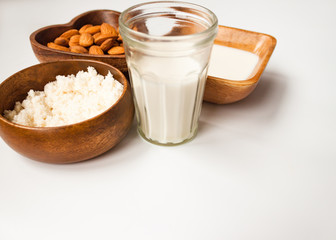 Homemade almond milk in a glass, almonds, milk and squeezed nut in wooden bowl on white background
