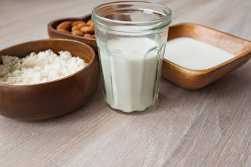 Homemade almond milk in a glass, almonds, milk and squeezed nut in bamboo bowl on wooden background