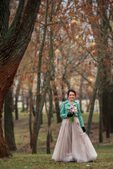 Obraz na płótnie Canvas Young beautiful girl in a long dress and a green jacket and with bouquet of flowers in her hands