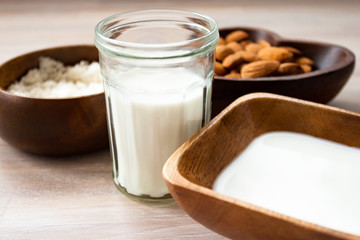 Homemade almond milk in a glass, almonds, milk and squeezed nut in bamboo bowl on wooden background