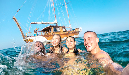 Young millennial friends taking selfie and swimming at sailing boat sea trip - Rich guys and girls...