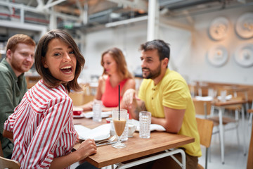 young woman smiles at camera in restauran with friends. Friendship and good time