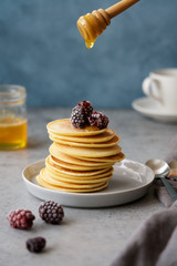 American pancake stack on wooden plate with rustic wooden backdrop. Blue linen and walnuts as decoration. Maple syrup on the sides and pour over pancakes. Food photography concept