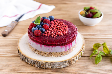  Raw dessert. Cake with berries on a wooden background. Raspberries and blackcurrants.
