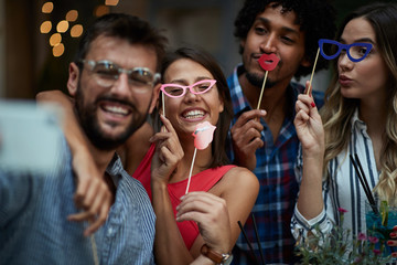 four young multiethnic adults having fun with props on sticks, Fun, joy, crazy, party, friends, couples, multiethnic concept