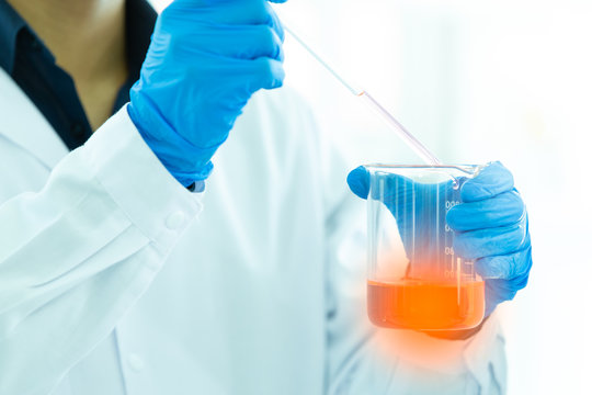 Close up Asian female scientist holding a tube and beaker with liquid substance, chemical in to beaker. Blurred background.