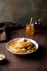 Stack of Crepes on plate with honey on wooden table. Traditional Russian thin pancakes on Masleniza