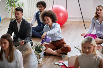group of business coworkers meditating at work, sitting on the floor, one female making visualization of money income increase. business, meditation concept