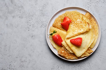 Stack of Crepes on plates on gray table with honey and fresh strawberries. Traditional Russian or French thin pancakes 