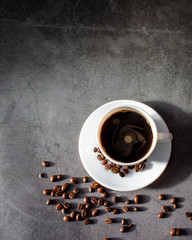 White cup with saucer and coffee beans, aromatic, hot coffee on a dark flat lay