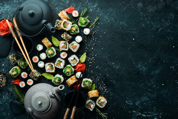 Sushi rolls and teapot with tea on black stone background. Great set of Japanese food