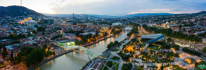 The evening panorama of the old town in the old district of Avlabari, Holy Trinity Cathedral and Rike Park, the Kura river reflects the evening city lights in Tbilisi, Georgia. © miklyxa