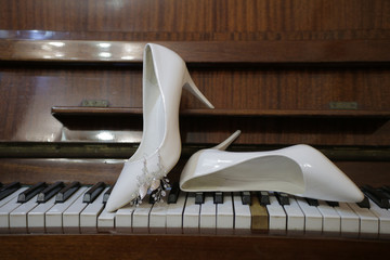 white women’s shoes on the piano keys, decorative earrings attached to the shoe