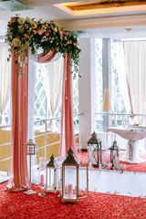 wedding arch draped with white and pink fabric, white and red flowers on the top, decorative lamps...