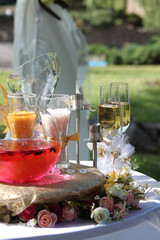 rose petals float in pink water in a glass spherical vase, white and yellow sand in glasses, two glasses with champagne, decor with white and pink roses