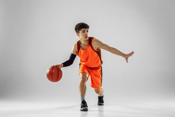 Naklejka premium Young basketball player of team wearing sportwear training, practicing in action, motion in run isolated on white background. Concept of sport, movement, energy and dynamic, healthy lifestyle.