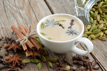 Cup of healthy ayurvedic masala tea or coffee with milk and aromatic spices. Cinnamon sticks, cardamom, cloves and anise stars on table.