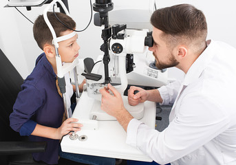 Male ophthalmologist checks eyesight of a teenage boy using a binocular slit-lamp. Checking...