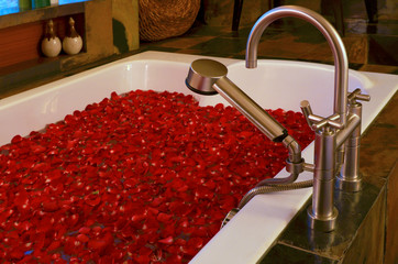 Luxury bathtub with many leaves rose on water, faucet.