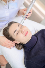 A woman lies on a couch in the office of a dermatologist and receives a cosmetic procedure. CO2 grinding of the skin of the face with the help of an apparatus.