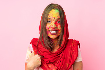 Young Indian woman with colorful holi powders on her face isolated on pink background with surprise facial expression