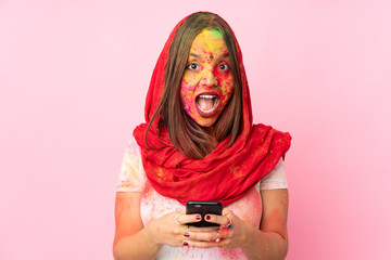 Young Indian woman with colorful holi powders on her face isolated on pink background surprised and sending a message