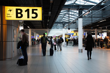 Airport terminal gate with gate number for departing flights, passengers waiting with luggage and suitcase 