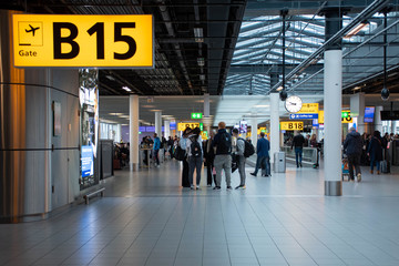 Airport terminal gate with gate number for departing flights, passengers waiting with luggage and...