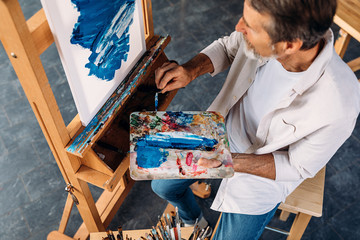 High angle view of male artist holding palette and paint knife