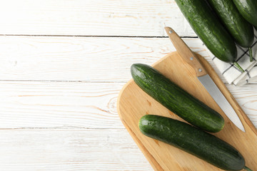Board and towel with cucumbers and knife on wooden background, space for text