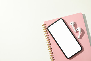 Phone with empty screen, headphones and copybook on white background, top view
