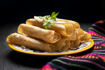 Mexican potato and cheese fried tacos also called flautas on dark background