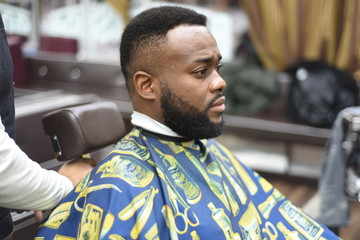 Black man in the Spanish barbershop. Cute black man makes a haircut in the African salon. Hair...