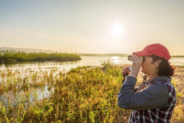 Woman looking through binoculars at summer sunny dawn.