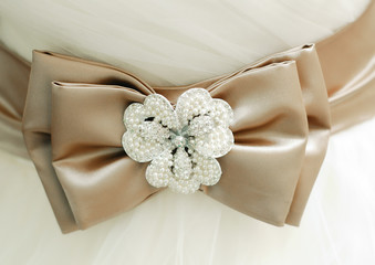 Coffee-colored satin bow with a flower brooch made of rhinestones on a white wedding dress