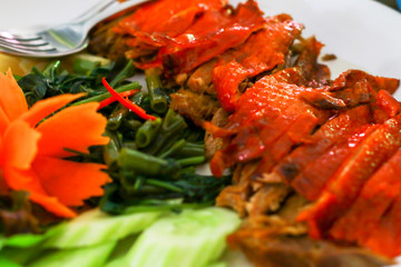 Famous Asian food roasted duck and boiled morning glory and fresh vegetables on the side in white plate.